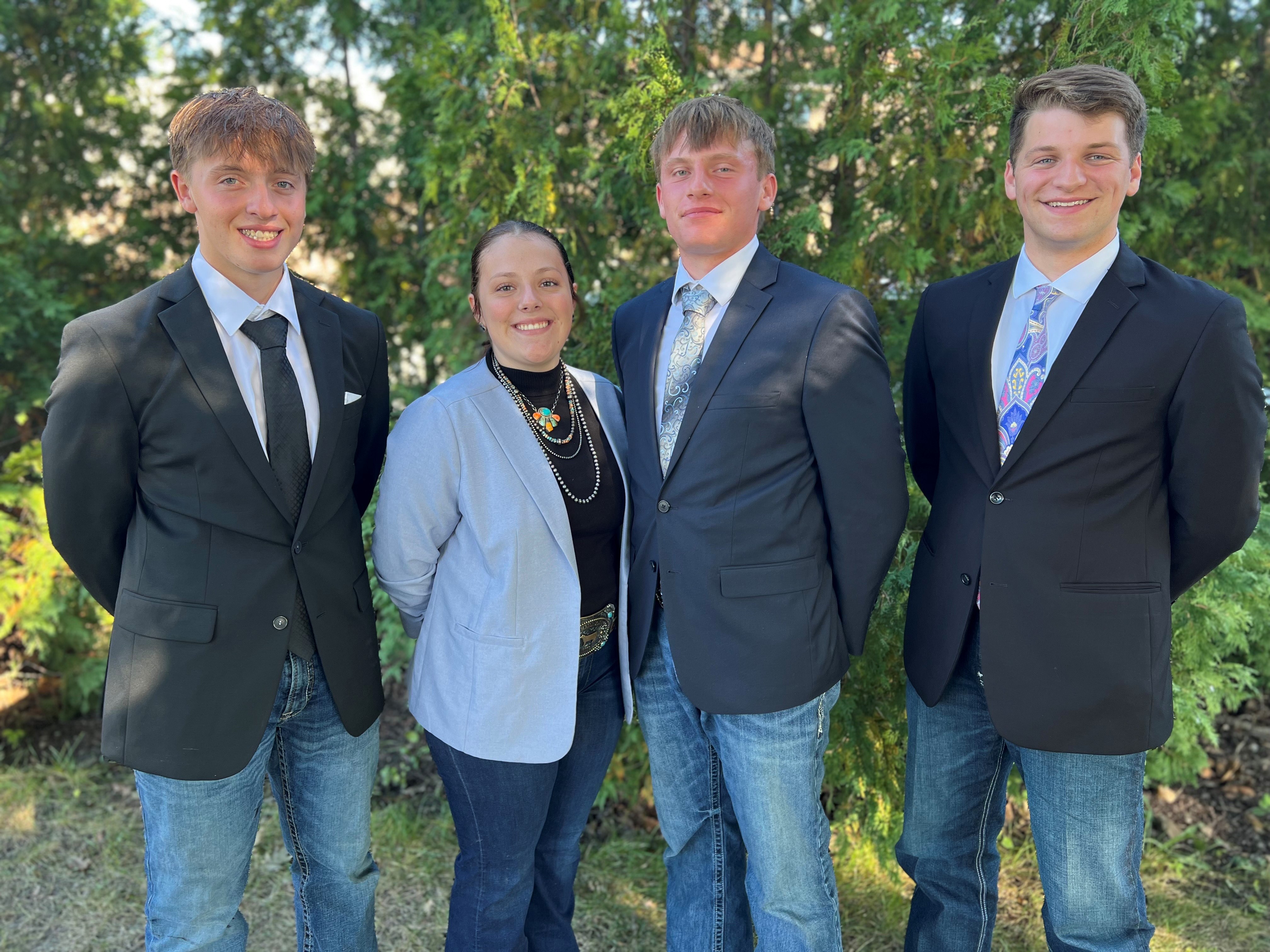 Four youth in blazers, one female and three males, in front of trees.